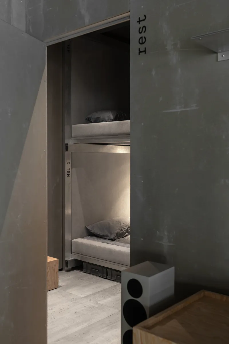 View into a sleeping alcove with stacked bunk beds and integrated lighting beside concrete walls