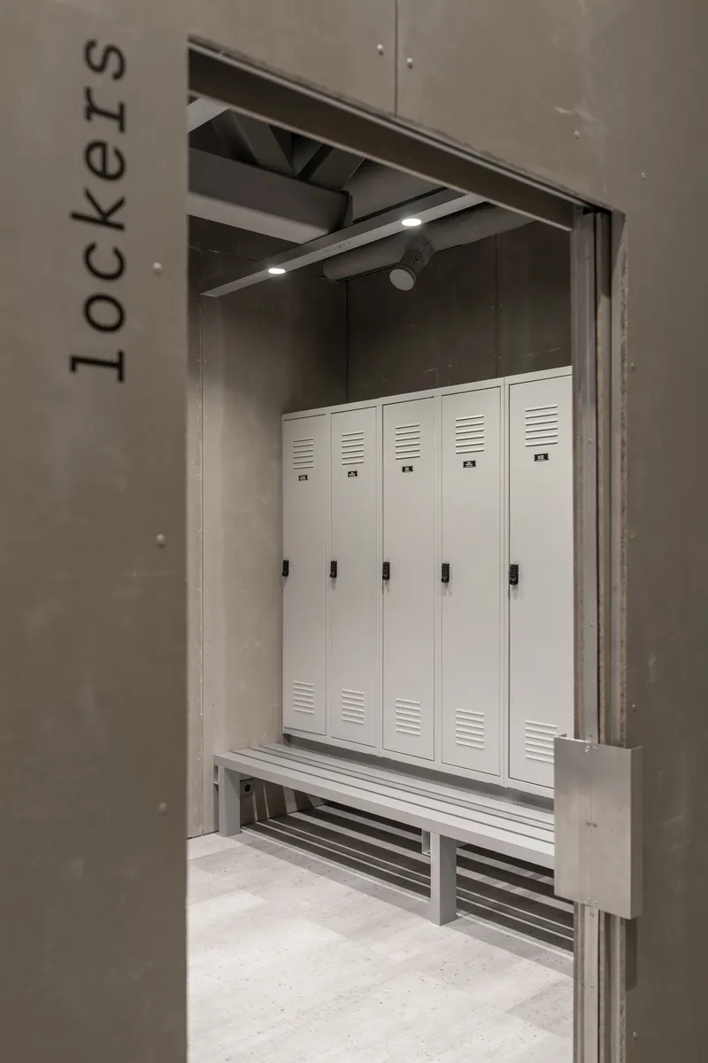Locker room entrance showing white metal lockers with benches beneath exposed ceiling fixtures