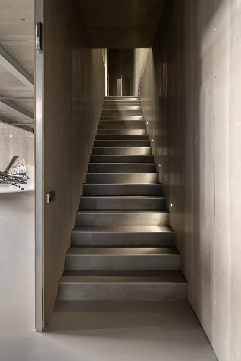 Narrow concrete stairwell with integrated step lighting ascending between dark walls