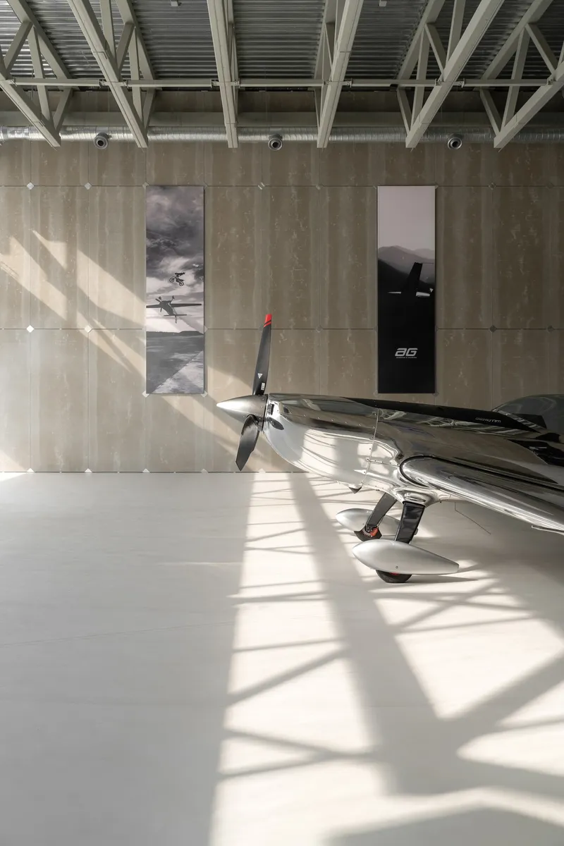 Aircraft hangar interior with board-formed concrete walls and exposed steel truss ceiling in bright daylight