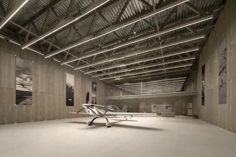 Long view down the hangar showing steel roof trusses and linear lighting above concrete walls
