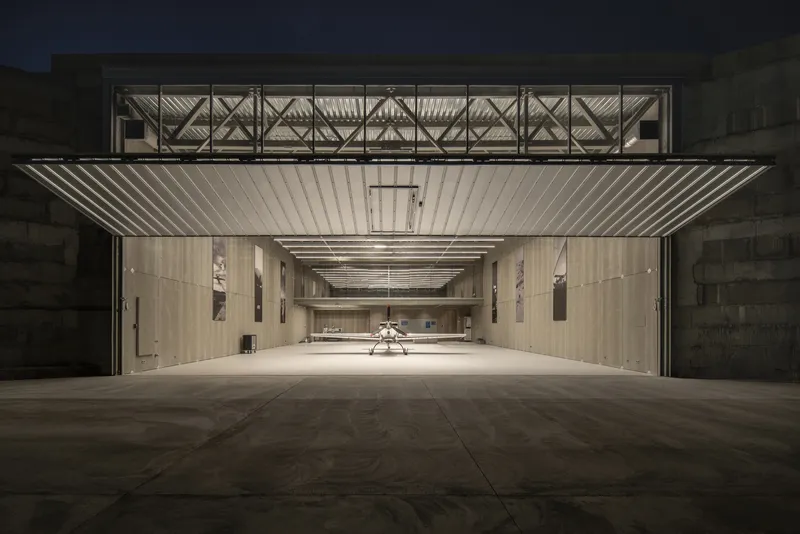 Exterior view of the open hangar door with corrugated metal soffit and exposed truss structure at dusk
