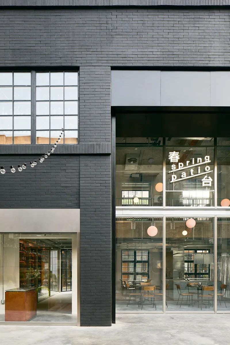 Dark grey brick facade with gridded glass block windows and a glazed cafe entrance with string lights