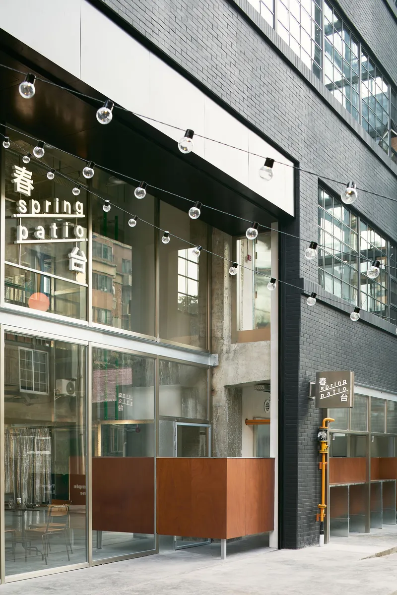 Cafe entrance beneath a dark awning with globe string lights and copper clad reception desk visible inside