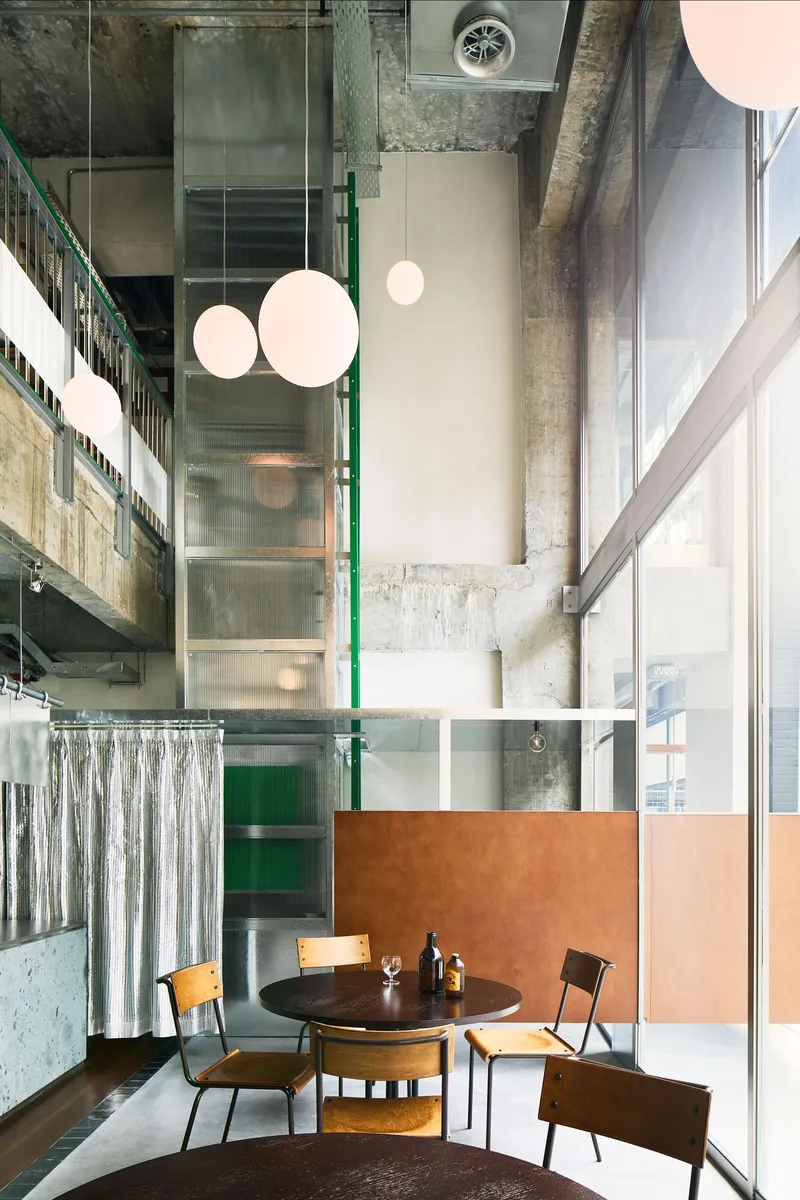 Dining area with copper panel partition, spherical pendant lights and exposed concrete columns framing full-height glazing