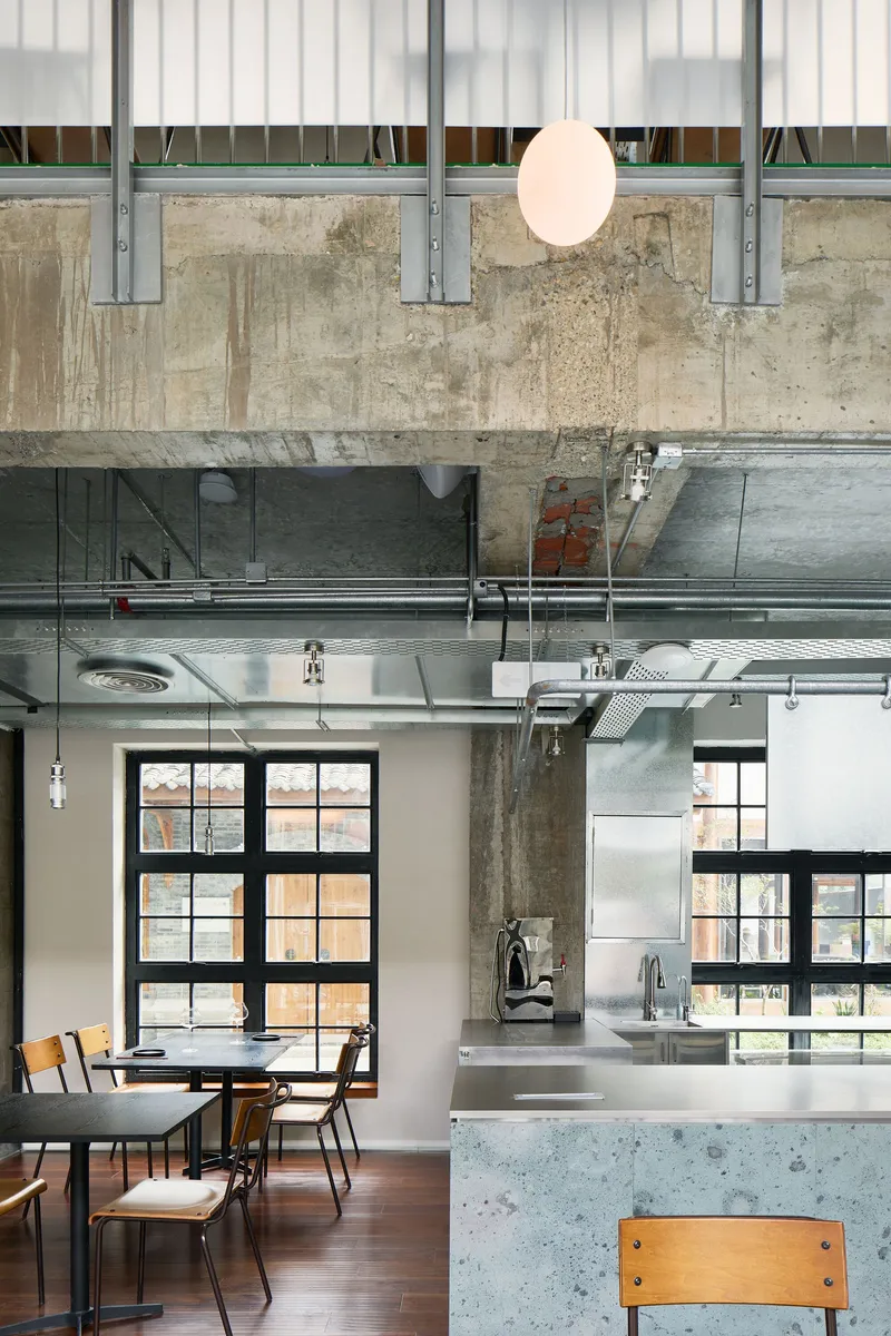 Interior space showing raw concrete ceiling, exposed ductwork and a single pendant light beside steel beams