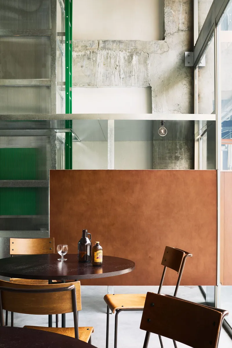 Seating area with copper partition panel against exposed concrete walls and green-framed translucent glass doors