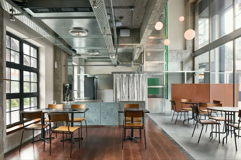 Interior dining space with exposed concrete ceiling, ventilation ducts, and pink globe pendant lights