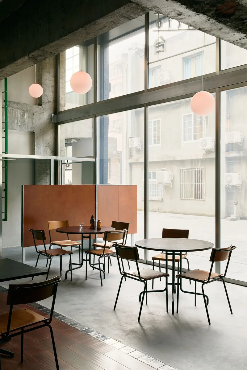 Double-height dining area with concrete ceiling, pink globe pendants, and copper-toned partition panels