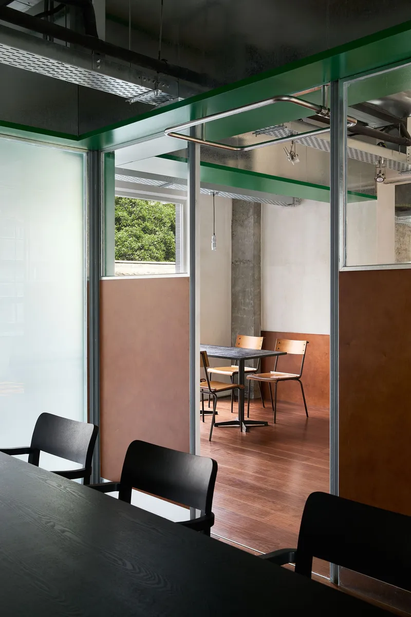 Seating booth framed by steel posts and glass partition with copper-clad lower wall panels