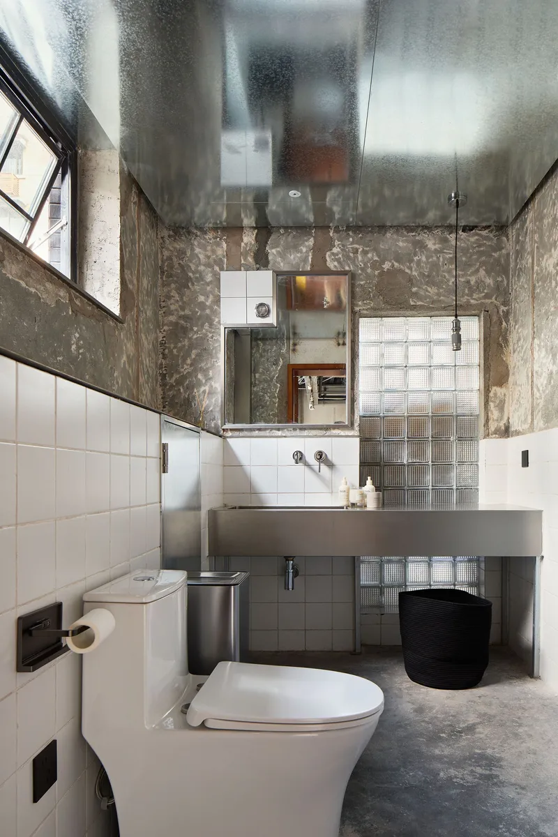 Compact bathroom with reflective metal ceiling and white tile wainscoting under textured concrete walls