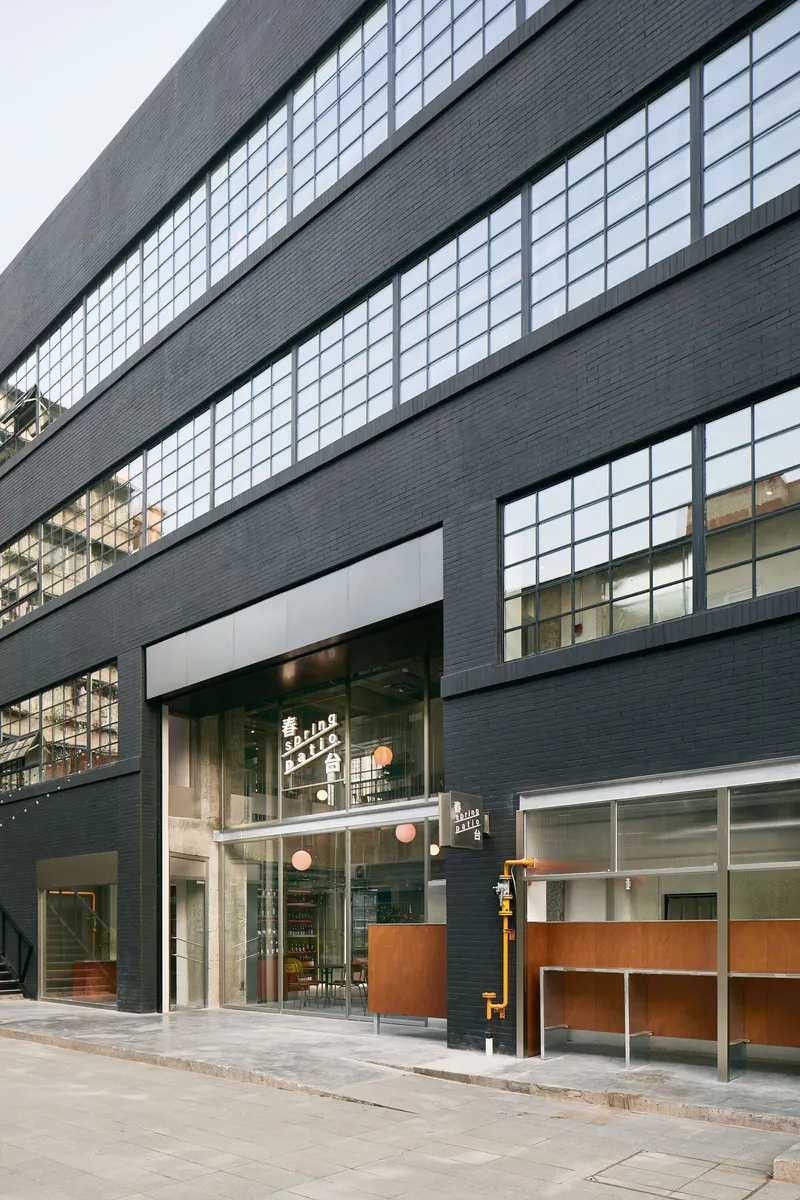 Street view of the dark brick facade with horizontal ribbon windows and double-height cafe storefront