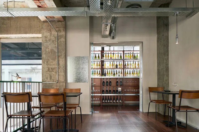 Backlit bottle display shelving viewed through exposed concrete columns and perforated metal ductwork