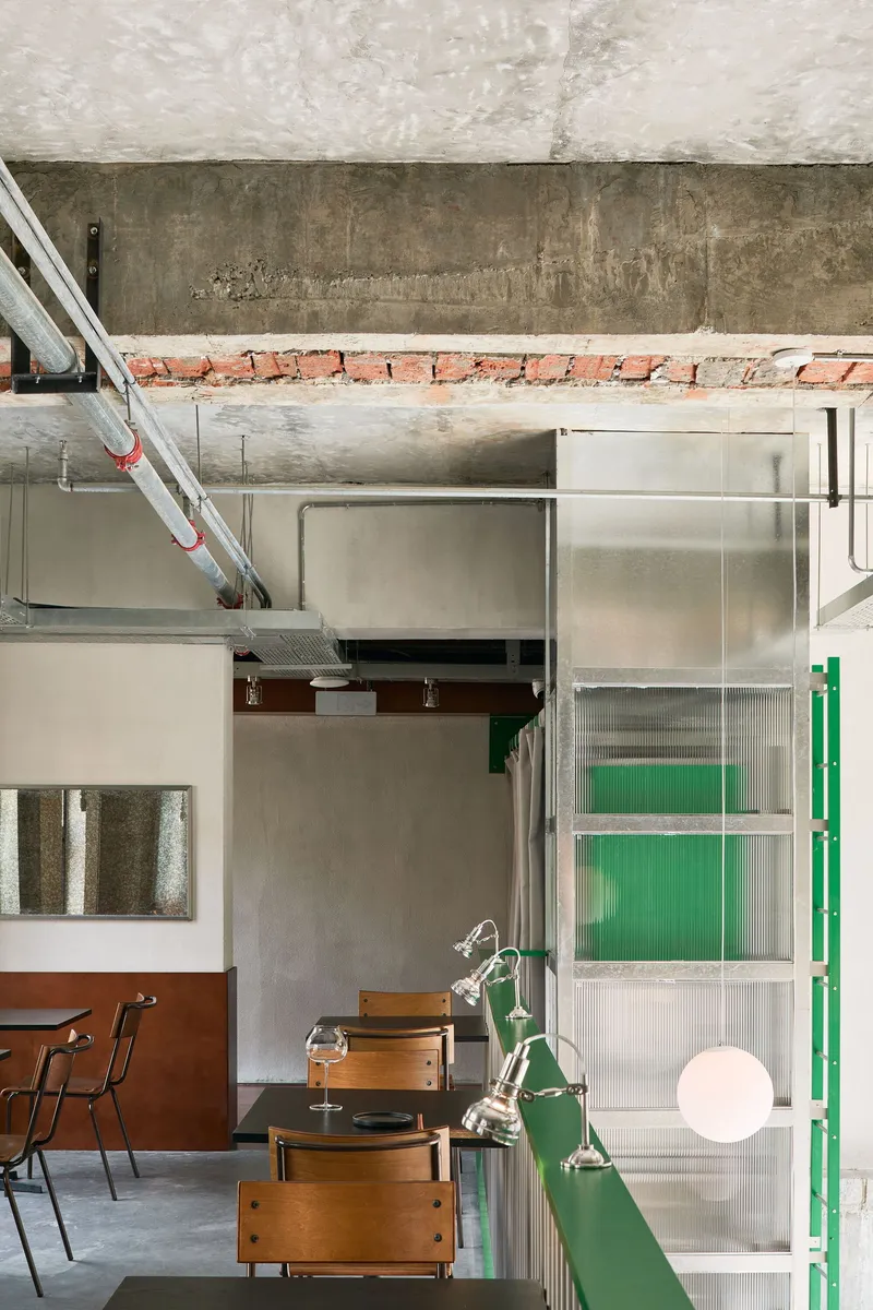Translucent panel partition with green frame meeting a concrete beam with exposed brick above
