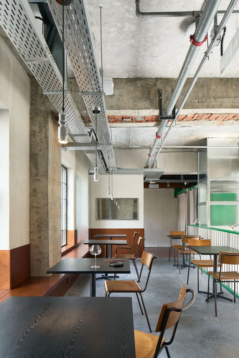 View across dining tables showing perforated metal ductwork suspended below concrete beams and brick