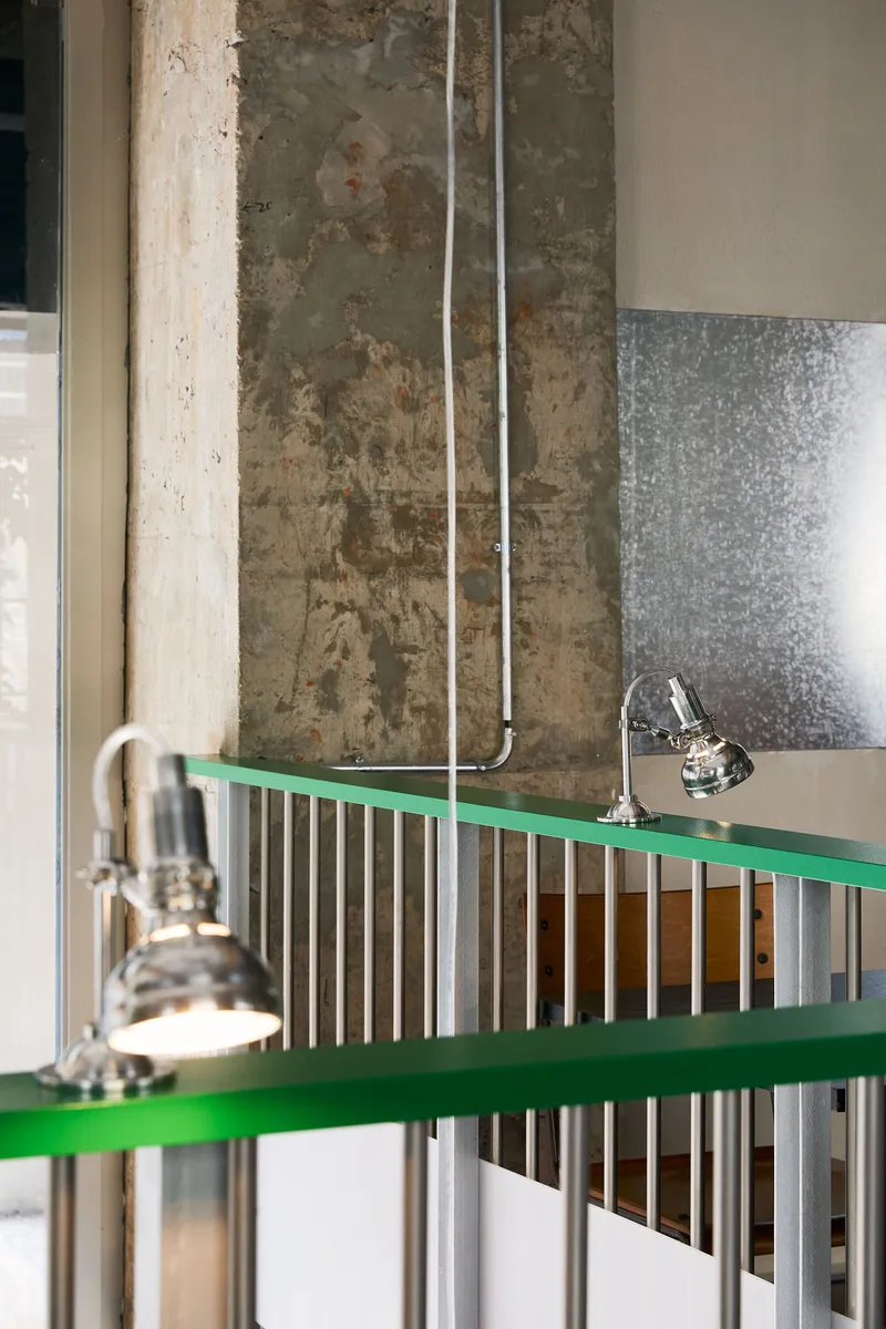Close-up of green metal railing with vertical corrugated infill against a weathered concrete column
