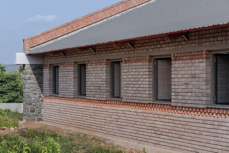 Exterior wall showing corrugated metal roof eave above perforated brick openings and exposed timber brackets