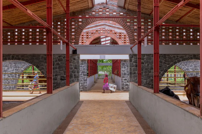 Interior passage with concrete ramp, red steel columns and brick archways framing figures and cattle outside