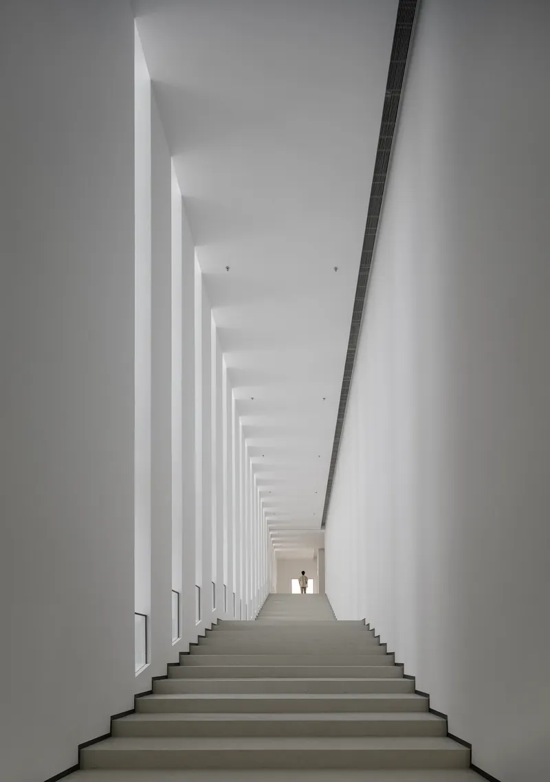 White staircase flanked by vertical columns of daylight with two figures silhouetted at the top