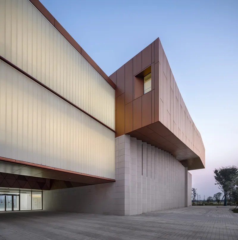 Junction between the light metal panel facade and the cantilevered bronze volume at twilight