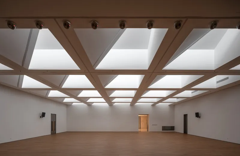 Gallery interior with timber grid ceiling and backlit skylights above a pale wood floor