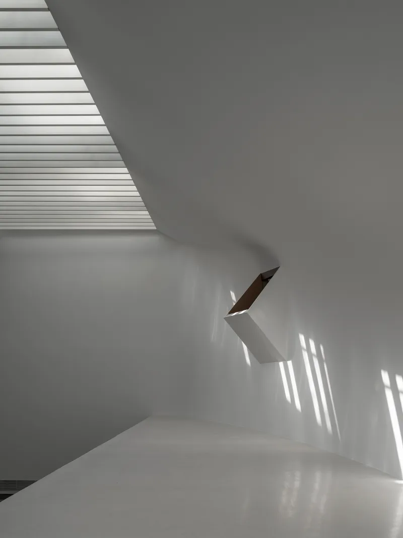 White interior staircase with timber handrail catching striped shadows from overhead louvers