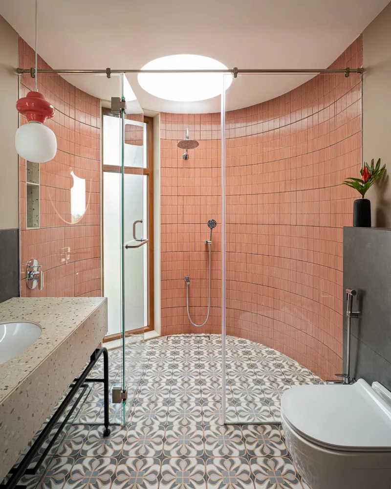 Curved coral tile shower enclosure with patterned floor tiles and oval skylight above