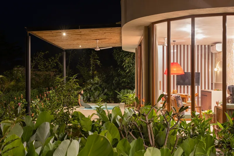 Night view of the glazed living room and timber-lined overhang framed by dense garden plantings
