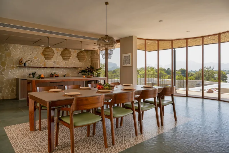 Dining room with timber table, woven pendant lights and full-height curved glass wall overlooking distant hills