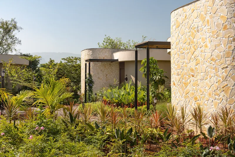 Curved stone-clad cylinders rising behind planted beds with palms and tropical foliage