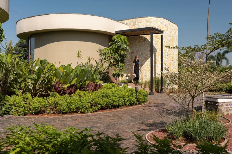 Entry path winding through planted beds toward cylindrical volumes under a metal canopy frame