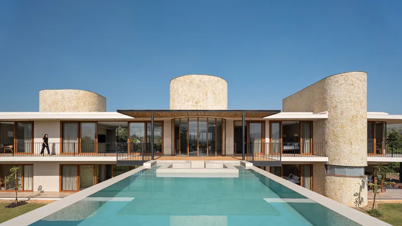 Rear elevation with three cylindrical stone towers flanking a glazed living volume and terrace over a reflecting pool