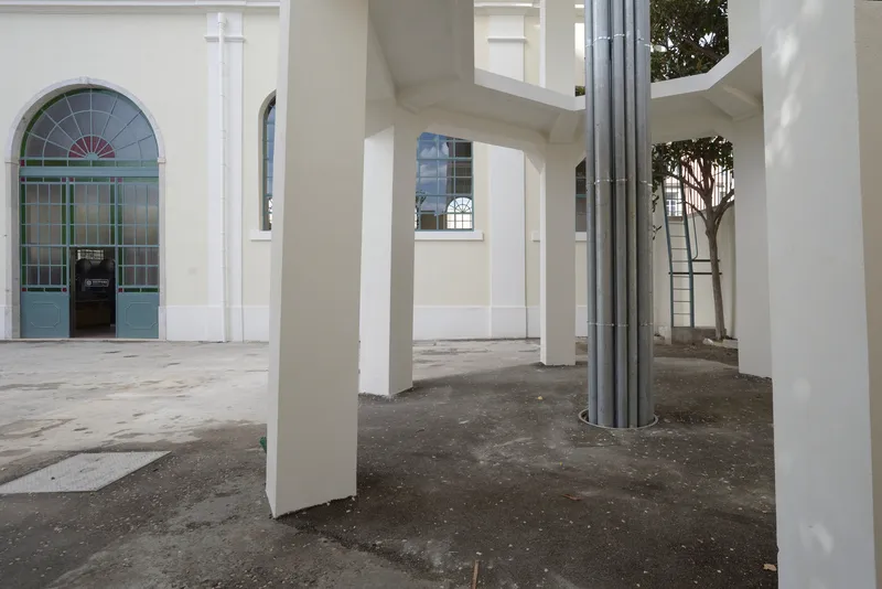 Covered arcade with white square columns and a circular metal duct wrapping around one pillar