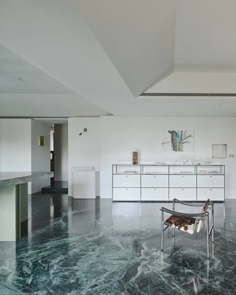 This architectural image showcases a modern and minimalist living room with a striking green marble floor. The space features white walls, a geometric ceiling,