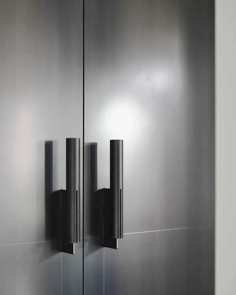 This image showcases a close-up of a modern, minimalist door with cylindrical metal handles. The gray metal surface reflects light, creating subtle gradients an
