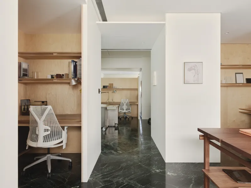 This architectural photograph showcases a modern interior with a minimalist aesthetic. The design features a compact office space with plywood shelving and a bu
