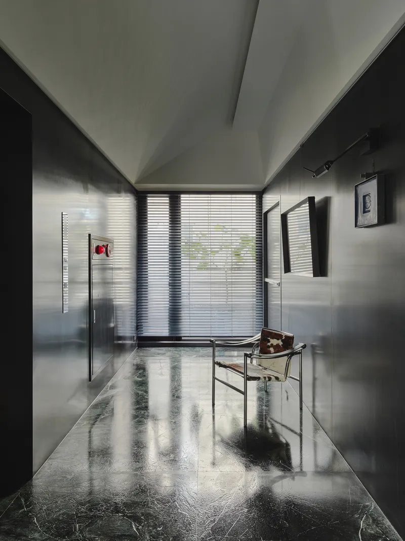 This architectural image showcases a modern hallway with a minimalist design. The space features polished marble floors, metal paneling, and a geometric ceiling