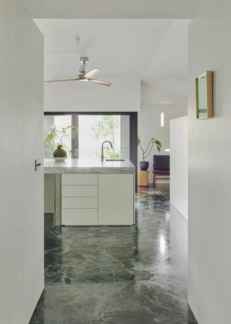 This architectural photo showcases a modern kitchen interior with a minimalist design. The space features a marble floor, a kitchen island with a marble counter