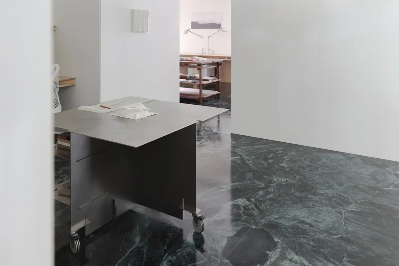 This architectural image showcases a minimalist studio space with a focus on clean lines and material contrast. The room features marble flooring, white walls,
