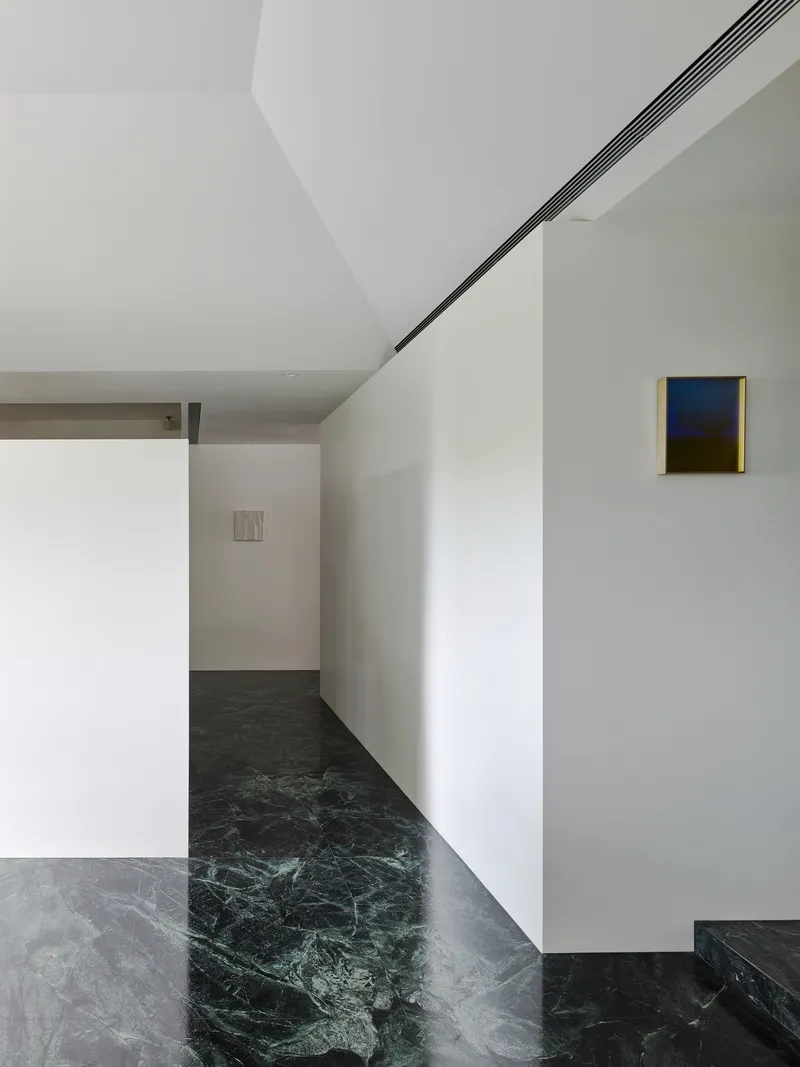 This architectural image showcases a minimalist hallway with white walls and a striking green marble floor. The space features clean lines, recessed lighting, a