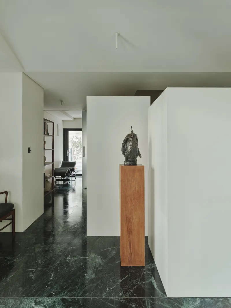 This architectural image showcases a modern interior with a minimalist design. The space features a hallway with green marble flooring, white walls, and a sculp