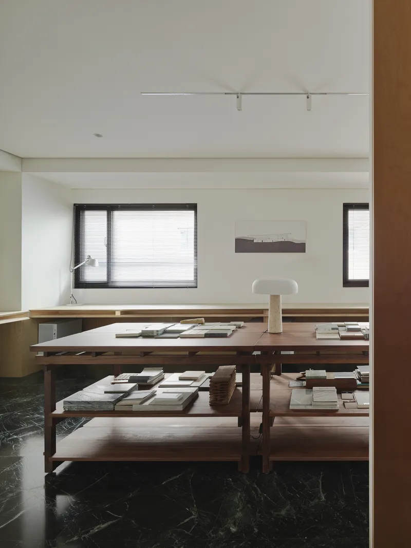 This architectural image showcases a modern interior design with a focus on clean lines and natural materials. The room features a large wooden table with shelv