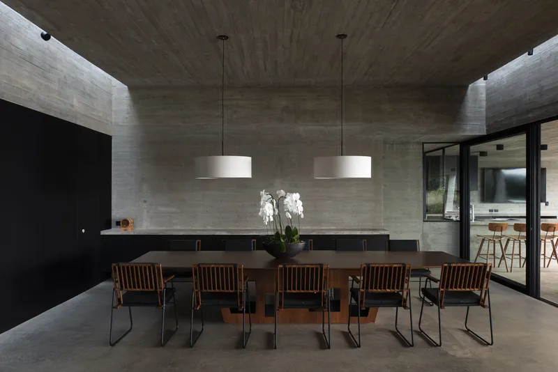 Dining room with boardmarked concrete ceiling and walls flanking a long table under pendant lights