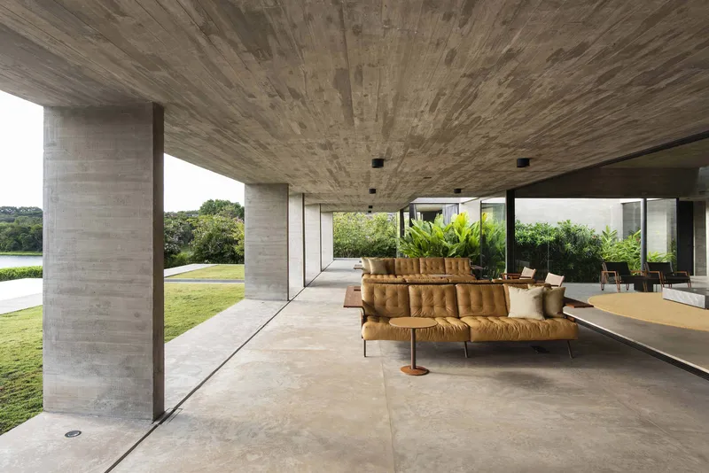 Covered terrace with boardmarked concrete ceiling and columns framing seating overlooking the lawn