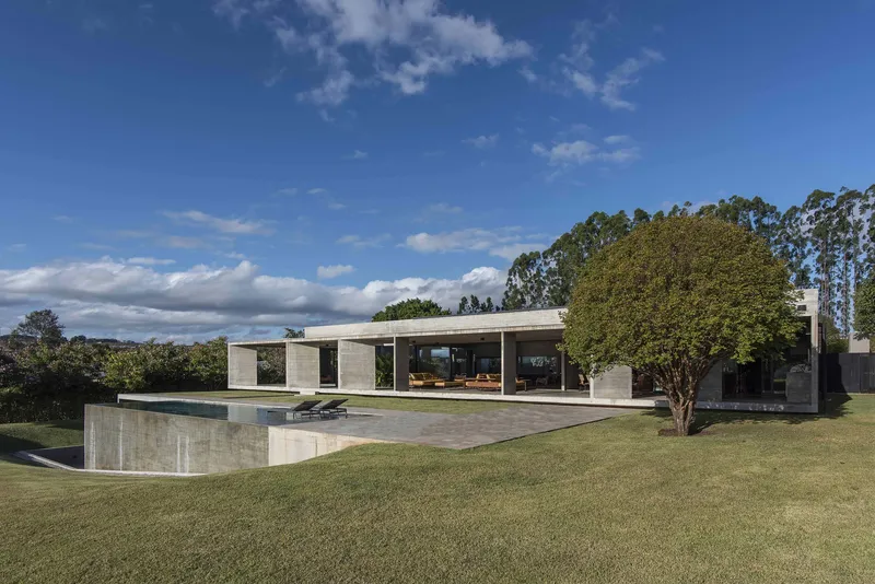 Concrete volume rising from a sloped lawn with terrace and mature tree in afternoon light