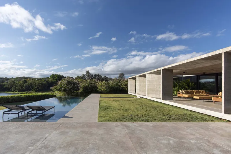 Infinity pool and covered terrace with formwork concrete ceiling overlooking lawn and distant wetlands
