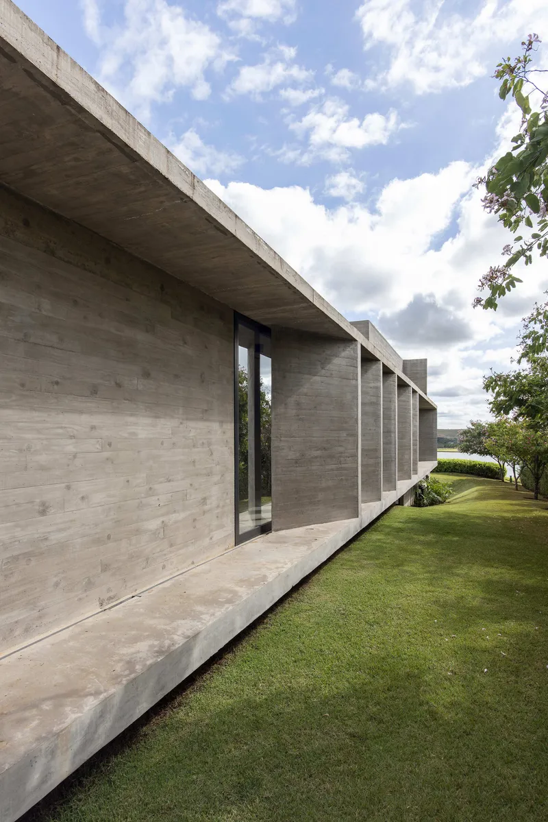 Board-formed concrete facade with vertical slot window and cantilevered roof slab against cloudy sky