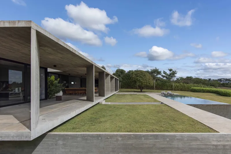 Covered terrace with exposed concrete columns framing a grass courtyard between pool and interior