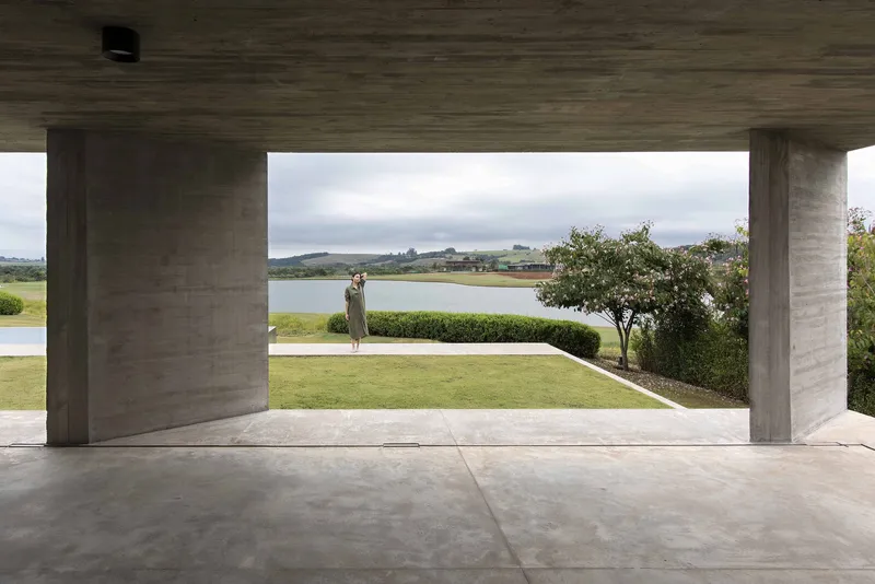 Covered terrace with board-formed concrete columns framing a view of the lawn and lake beyond