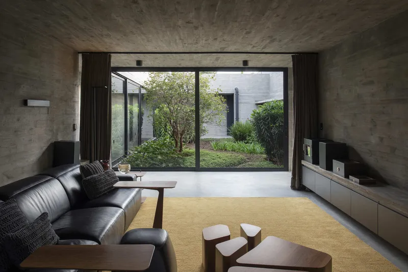 Living room with board-formed concrete walls and glazed doors revealing a courtyard garden with trees